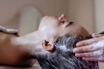 Naklejka premium Close-up of a Japanese Head Spa Treatment: Woman Relaxing While Receiving Scalp Massage with Hair Cleansing and Care in Beauty Salon