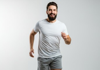 A bearded man in a white t shirt and gray shorts running and smiling against a white background