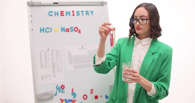 Chemistry teacher in blazer takes out test tube with liquid reagent from beaker with empty test tubes. Woman explains scientific experiment at lesson