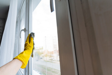 A person wearing bright yellow gloves is diligently cleaning a window using a soft cloth to ensure...