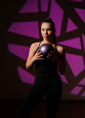 Woman showcases rhythmic gymnastics skills while holding a ball under dramatic lighting