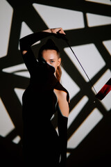 Woman performs rhythmic gymnastics with ribbon against an artistic backdrop of shadows