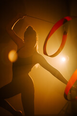 Woman trains in rhythmic gymnastics at an indoor venue during a dramatic lighting setup