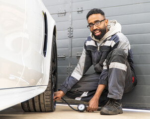 An African-American tire fitter inspects a car by measuring the tire pressure of the car. Mechanic...