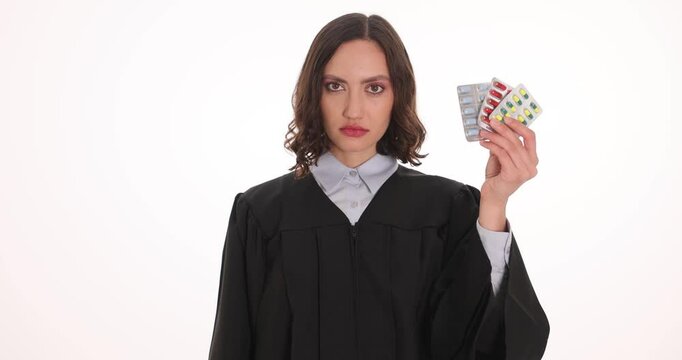 Female judge holds pills blisters and handcuffs on white background. Magistrate warns about prohibition and punishment for narcotic trafficking