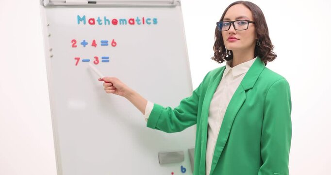 Woman teacher explains math problems on whiteboard. Female pedagogue shows addition and subtraction tasks at primary school lesson slow motion