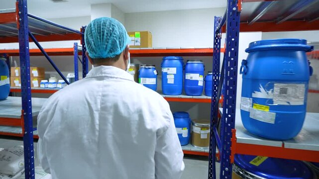worker in warehouse with container racks for storage and epoxy flooring in a pharmaceutical manufacturing factory. working in cleanroom for active pharma ingredients, speciality chemicals.	