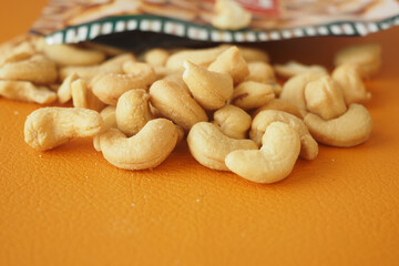 Cashew nuts spilling from an open bag on orange surface