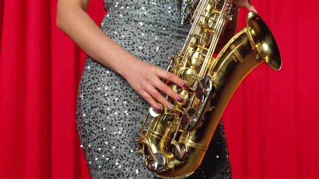 Close-up of female musician in elegant glamour dress playing alto saxophone, passionately improvising and performing live music on stage in concert hall.