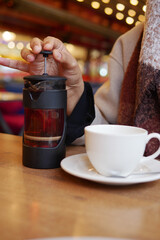 A person prepares tea using a French press while enjoying a warm beverage