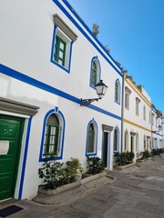 A view of traditional Canarian houses with blue and white facades, iconic green windows, and a street lamp, showcasing the architectural beauty typical of the Canary Islands’ residential areas.