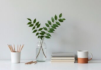 This image captures a tranquil home office arrangement with vibrant green foliage in a clear vase, organized pencils, stacked books, and a modern mug on a white desk