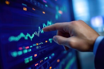 Close-up view of a hand pointing to stock market data on a display screen.