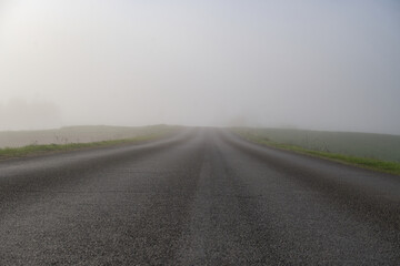 Misty road stretches into the distance, disappearing into a thick layer of atmospheric fog.
