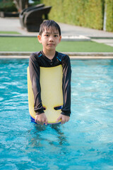 Thai Boy Practising Swimming with a Kickboard in Pool