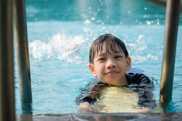 Thai Boy Practising Swimming with a Kickboard in Pool