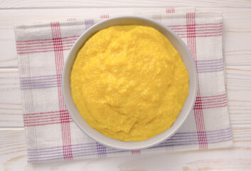 Delicious corn porridge in a bowl on a white wooden table.