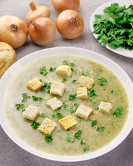 Homemade cream soup with chicken and herbs in a white plate on a gray background.