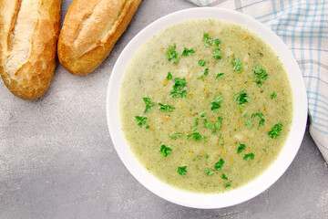 Homemade cream soup with chicken and herbs in a white plate on a gray background.