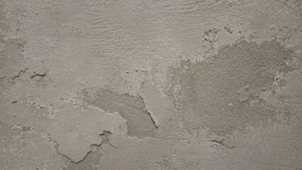 A close-up of a rough, worn-out concrete wall with a gritty texture, featuring cracks and crevices. The color is a dull, muted gray with subtle variations in shade, showing off the uneven surface.