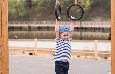 Lifestyle. A cute little boy is hanging on rings on a sports field in the fresh air. The concept of...