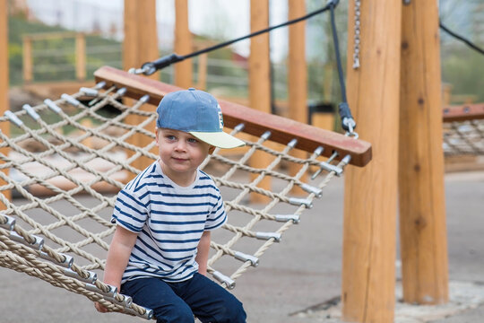 Lifestyle. A cute little boy is sitting in a hammock on a modern outdoor playground. The concept of family entertainment and leisure.