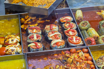 Assorted Turkish stuffed vegetables and stews in a restaurant display. A variety of traditional dishes in rich sauces, served hot and ready to eat.