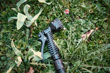 Close-up of a garden hose nozzle lying on green grass with leaves around