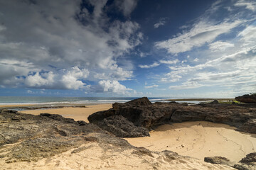 Rocky coastal landscape with dramatic clouds over a sandy beach, rocks, and crashing ocean waves. Beautiful nature scene.