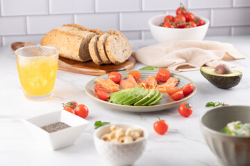 Healthy food composition with multigrain bread, avocado, salmon and tomatoes in a bright kitchen. Modern and clean style. Natural eating, slow living lifestyle