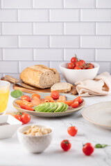 Marble table with a plate of avocado and cherry tomatoes. Background with whole grain bread, tomato bowl, and soft cloth. Fresh and balanced composition. Concept of healthy food and natural lifestyle