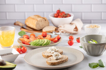 Healthy breakfast on marble table: whole-grain toast with avocado, smoked salmon, and orange kombucha. Nutrient-rich spread with cottage cheese, cherry tomatoes, and fresh ingredients against a bright