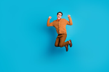 Obraz premium Excited young man jumping in joy against a vibrant blue background