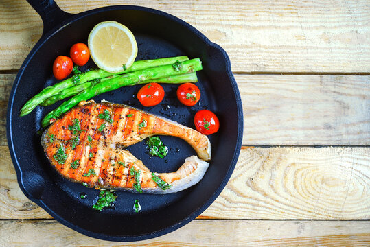Overhead view of a Grilled salmon steak with tomatoes,  asparagus and lemon in a frying pan