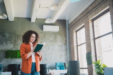 Young professional woman reading a book in a modern office interior featuring daylight and greenery