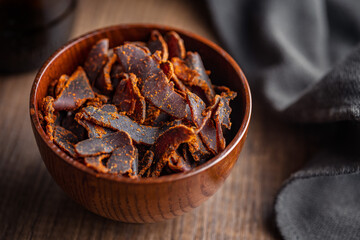 Beef jerky. Dried spiced meat in bowl on wooden table.