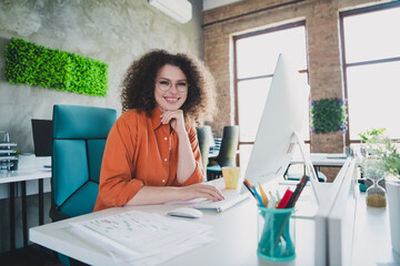 Confident businesswoman with curly hair working at modern office desk in a daylight-filled workspace