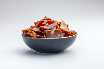 Beef jerky. Dried spiced meat in bowl on gray background.