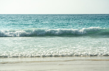 Clear turquoise waves gently crashing on a peaceful sandy beach at a tropical island coastline