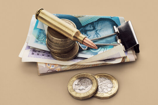 UK Defense Spending - still life of bullet cartridge and coins on stack of British money pounds
