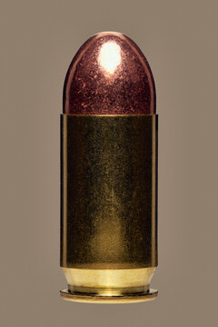 Close up studio shot of shiny .45 bullet on brown background
