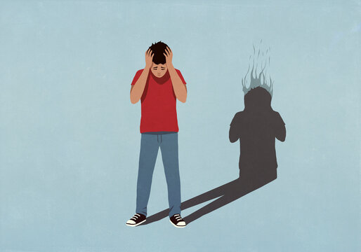Shadow with burning head behind frustrated boy with head in hands
