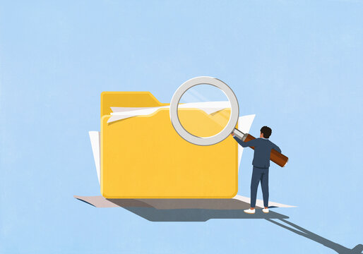 Businessman holding large magnifying glass over large messy file folder with paperwork
