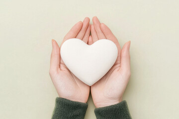 pair of hands gently holding white heart shaped object, symbolizing love and care, set against soft green background. This heartwarming scene evokes feelings of warmth and affection
