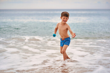 Happy boy playing in the ocean waves during summer vacation