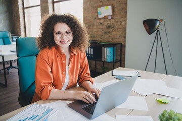 Young professional woman with curly hair working on a laptop in a modern office environment