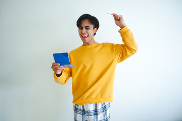 Happy Asian man holding a savings book with a proud face, looking at it with joy, symbolizing...