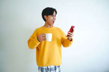 Excited Asian man holding a glass and using mobile phone with happy expression, isolated portrait...