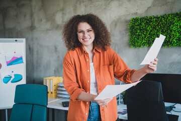 Young professional woman with curly hair in a modern office holding documents, demonstrating...
