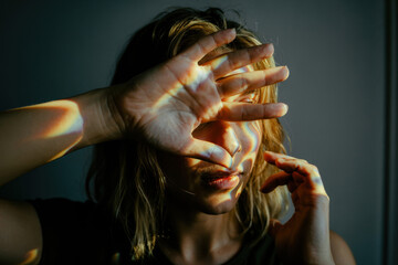 Introspective Woman Partially Concealing Face with Hand Under Soft Rainbow Light in Moody Atmosphere